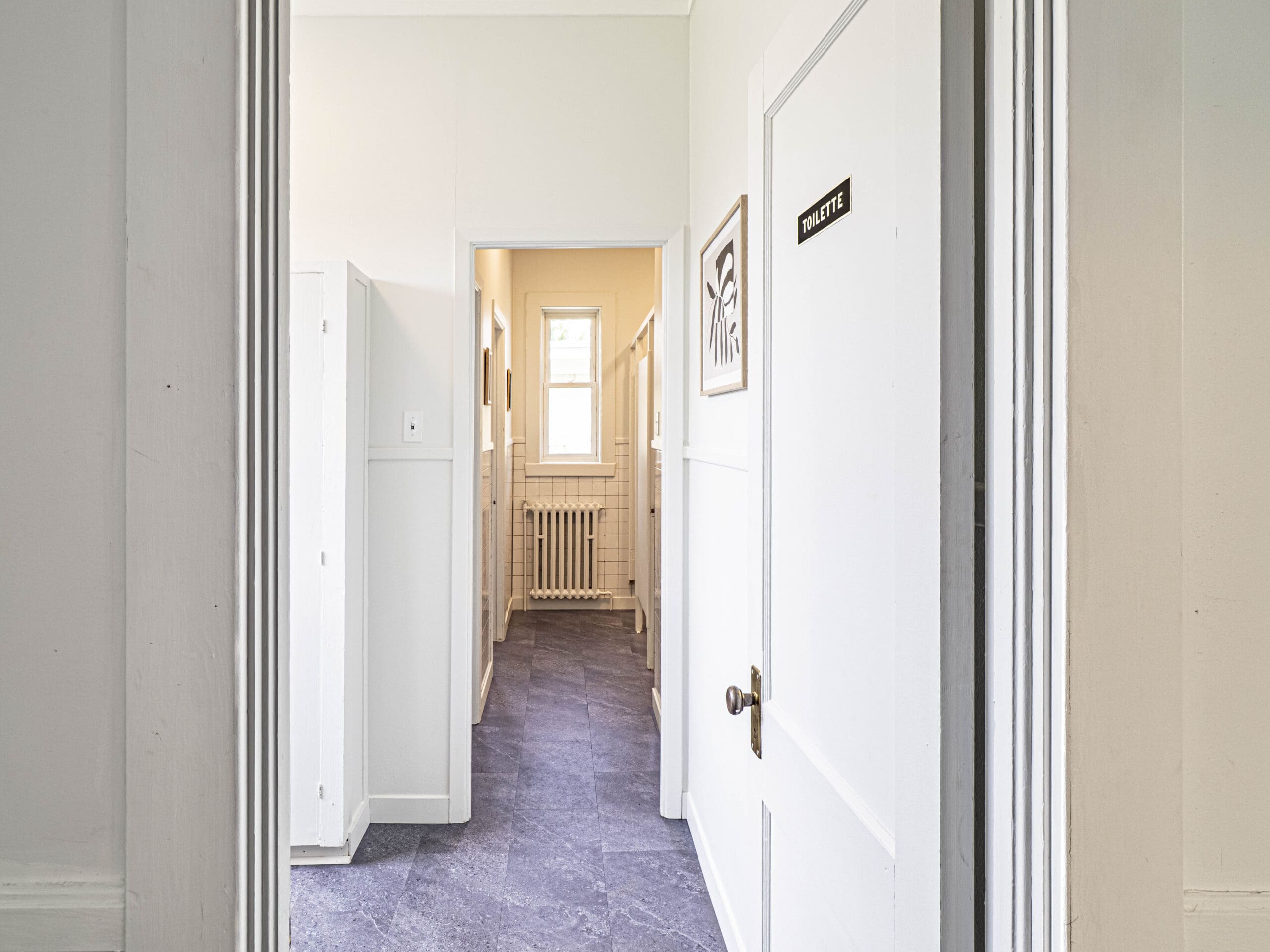 Un couloir lumineux avec un sol violet, des murs blancs et une porte portant l'inscription 